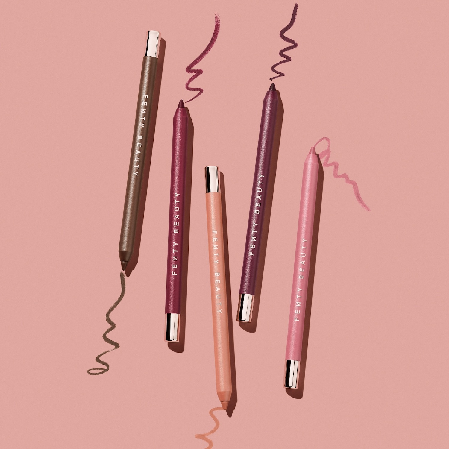 Découvrez les crayons à paupières Fenty Beauty, présentés dans des teintes marron, prune, pêche et rose, chacun laissant une trace de couleur crémeuse.