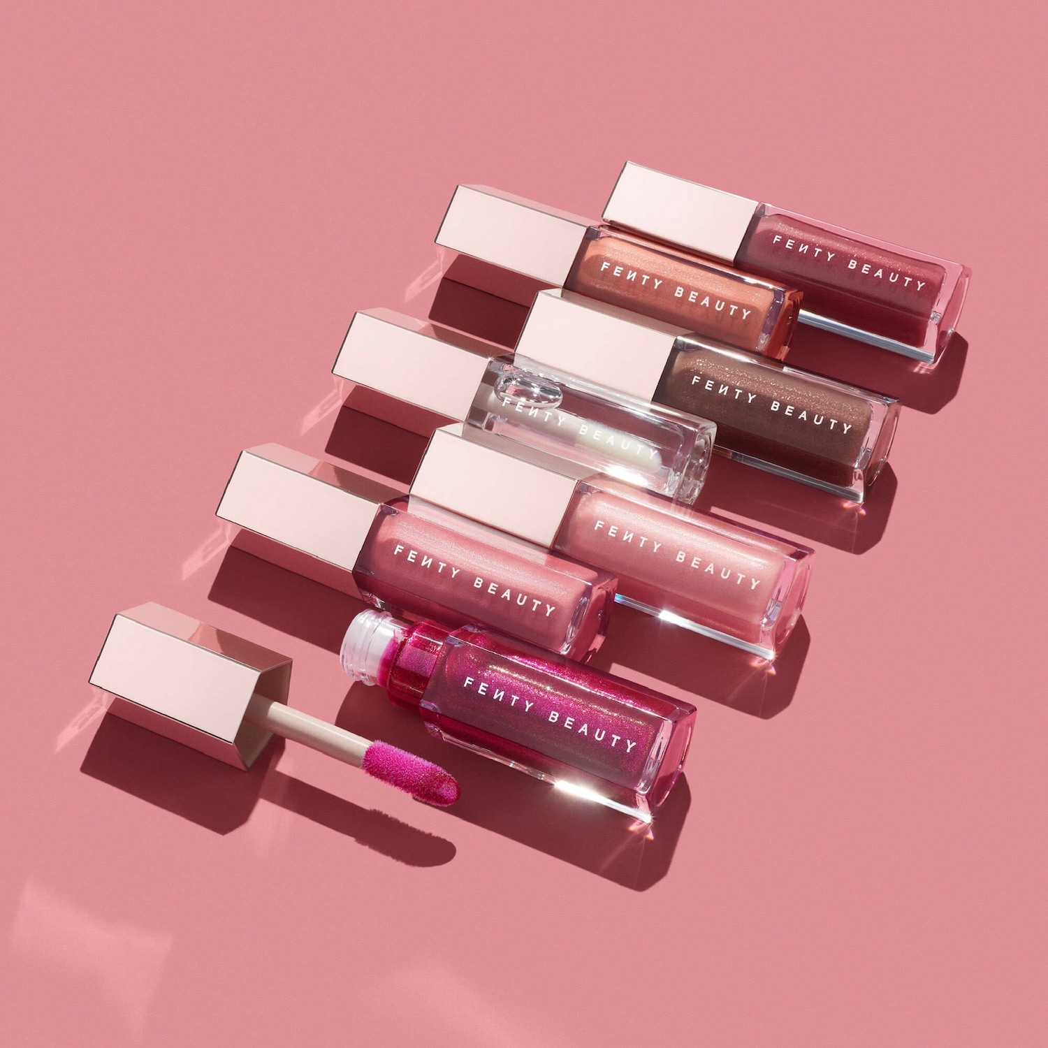 Découvrez une gamme de brillants à lèvres Fenty Beauty aux teintes chatoyantes, présentés dans des tubes transparents avec des bouchons rose pâle.