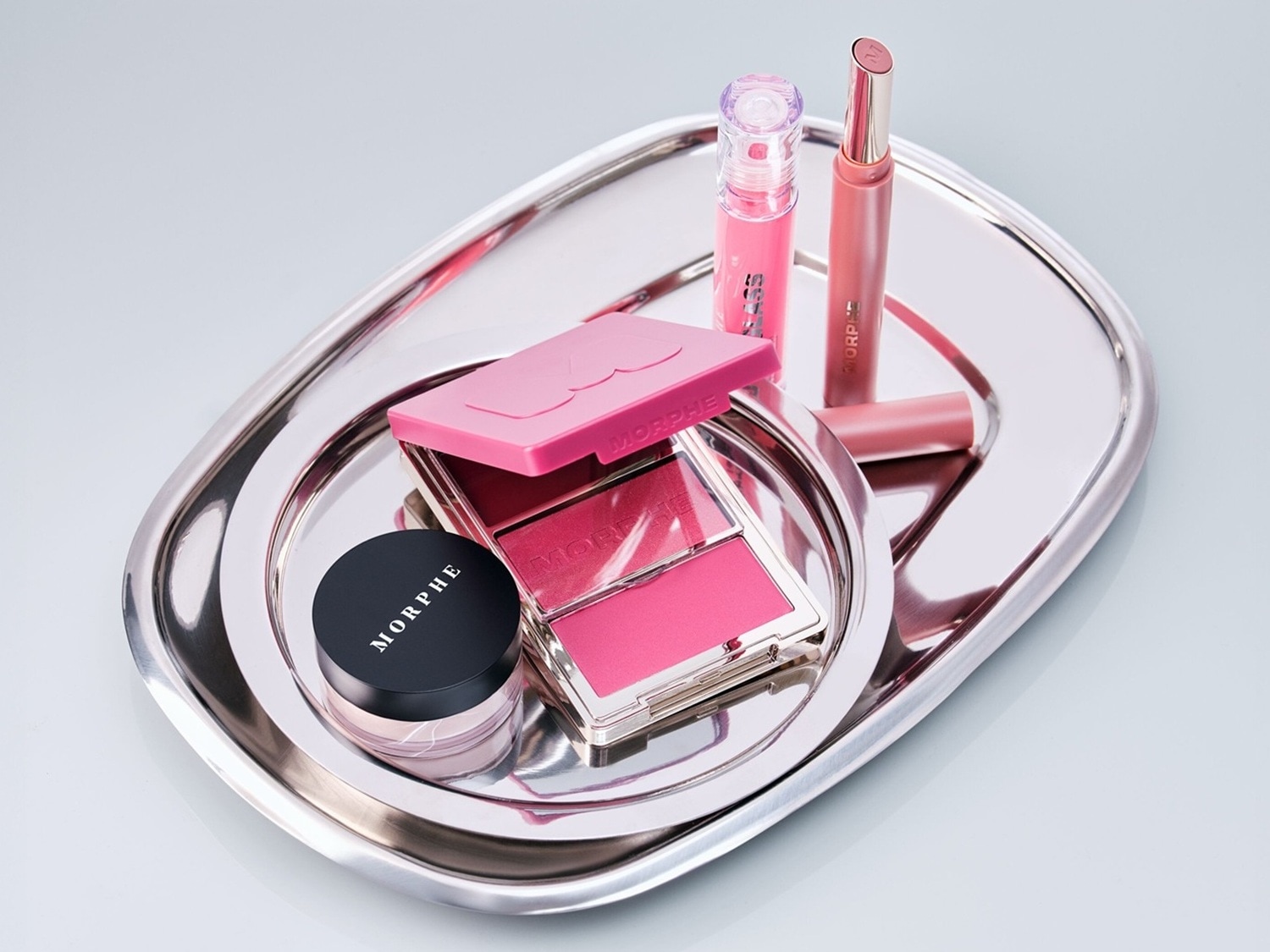 Auf einem silbernen Tablett sind verschiedene Make-up-Produkte von Morphe in Rosatönen angeordnet, darunter ein Rouge-Duo, ein Lipgloss und ein Lippenstift.