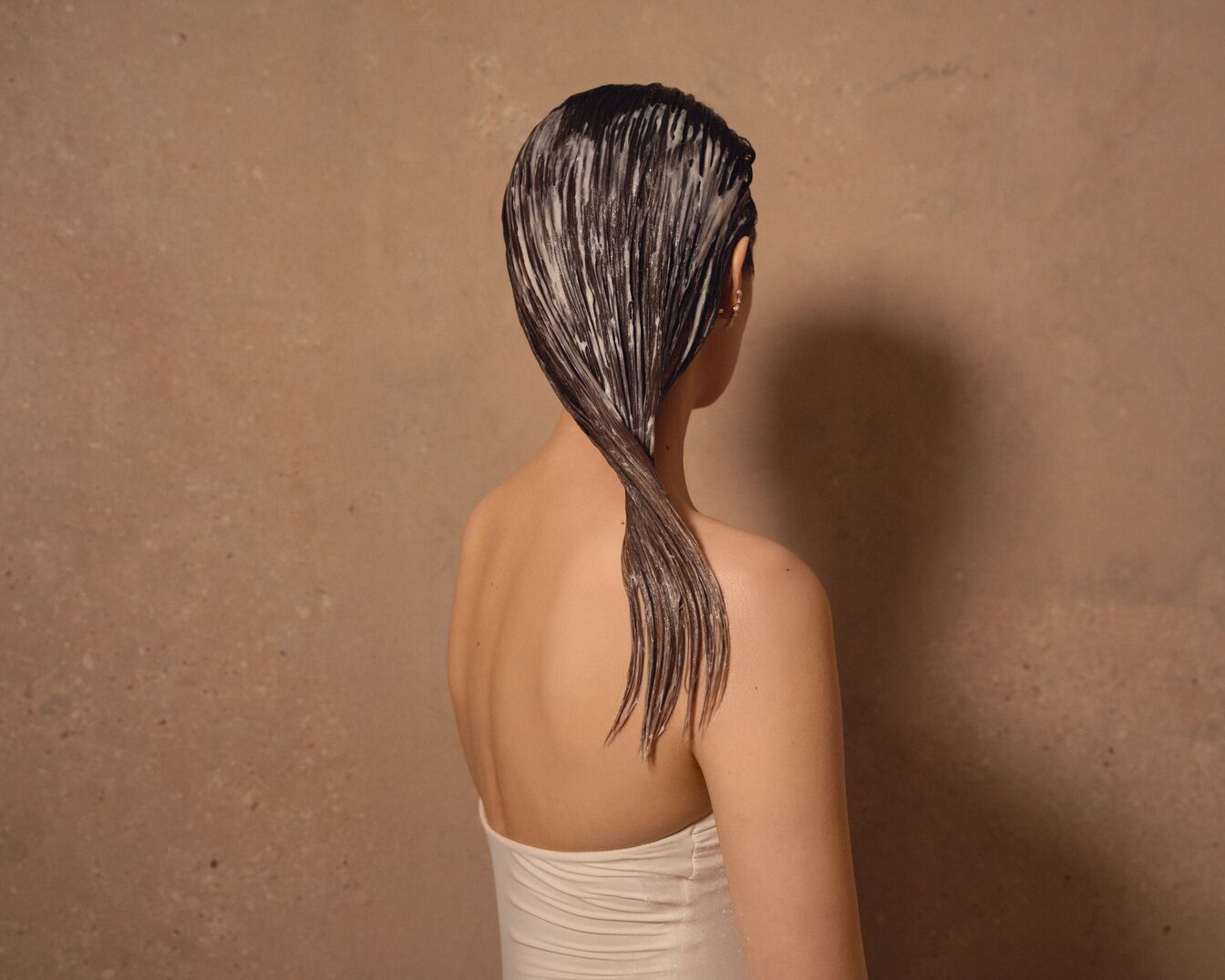 Nugaros vaizdas į moterį, tepančią plaukus kondicionieriumi, plaukai surišti į uodegą, o kondicionierius padengtas ant plaukų.