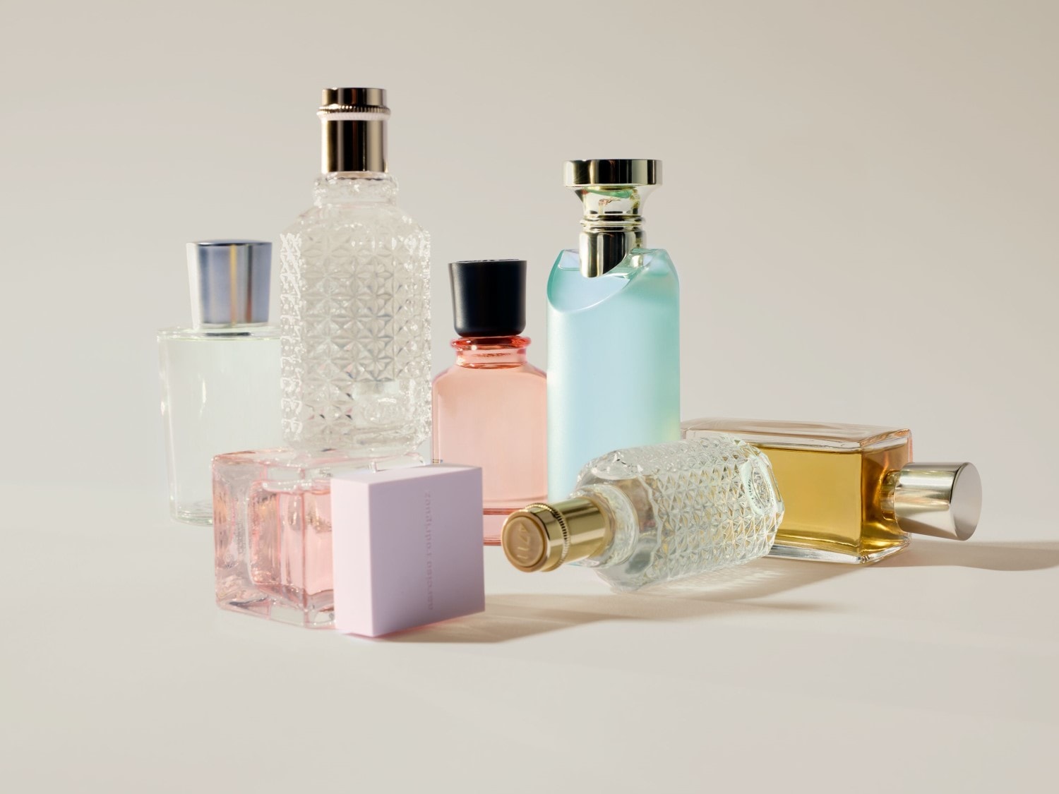 Eine Sammlung von Parfümflaschen in verschiedenen Formen und Farben, darunter klare, rosa, blaue und goldene Töne, die ein luxuriöses und vielfältiges Dufterlebnis versprechen.