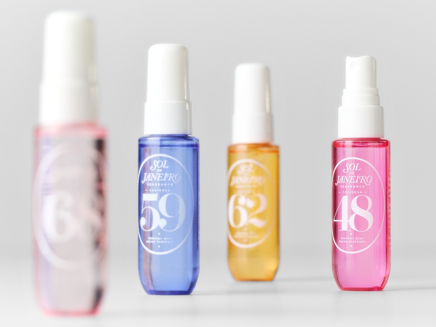Entdecken Sie die Sol de Janeiro Duftkollektion: Vier farbenfrohe Parfüm-Sprays in Rosa, Blau, Gelb und Pink, jedes mit einer einzigartigen Nummer und dem Sol de Janeiro Logo.