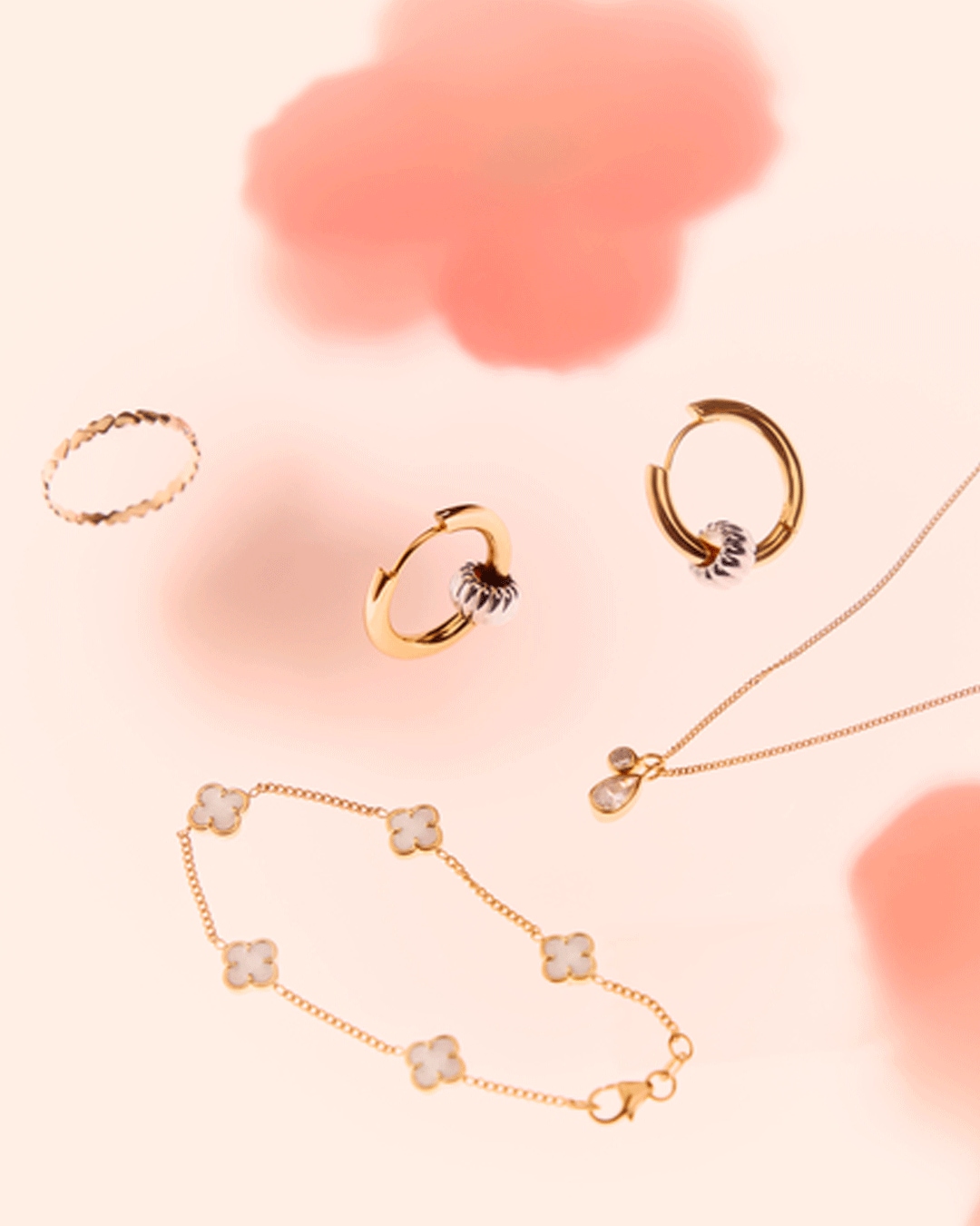 Entdecke eine Kollektion aus goldenem Schmuck, darunter Ohrringe, eine zarte Halskette, ein Armband mit Kleeblattmotiven und ein schlichter Ring, die auf einem sanften, rosafarbenen Hintergrund schweben.