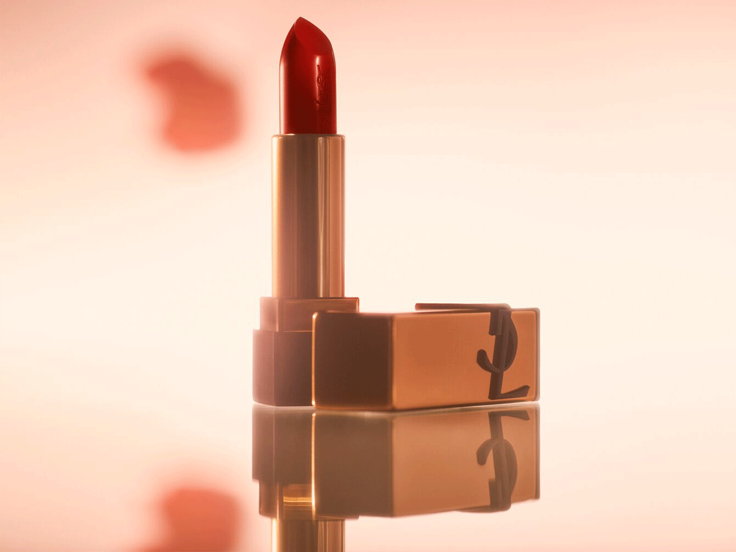 Ein roter Lippenstift von Yves Saint Laurent steht neben seiner goldenen Verpackung, die das ikonische YSL-Logo trägt.