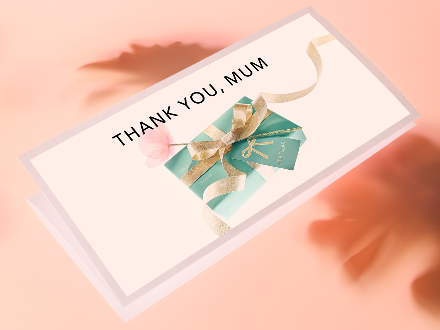 Eine Geschenkbox von Douglas in Mintgrün mit goldener Schleife und Anhänger, präsentiert auf einer Karte mit der Aufschrift "Thank You, Mum".