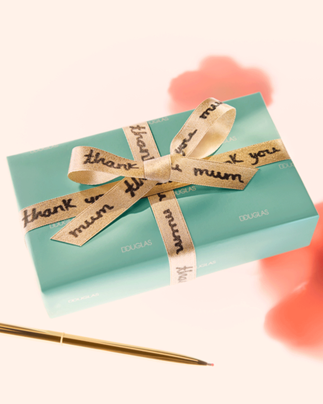 Ein helltürkisfarbenes Geschenk ist mit einem goldenen Band umwickelt, auf dem "Thank you Mum" steht, daneben liegt ein goldener Stift.