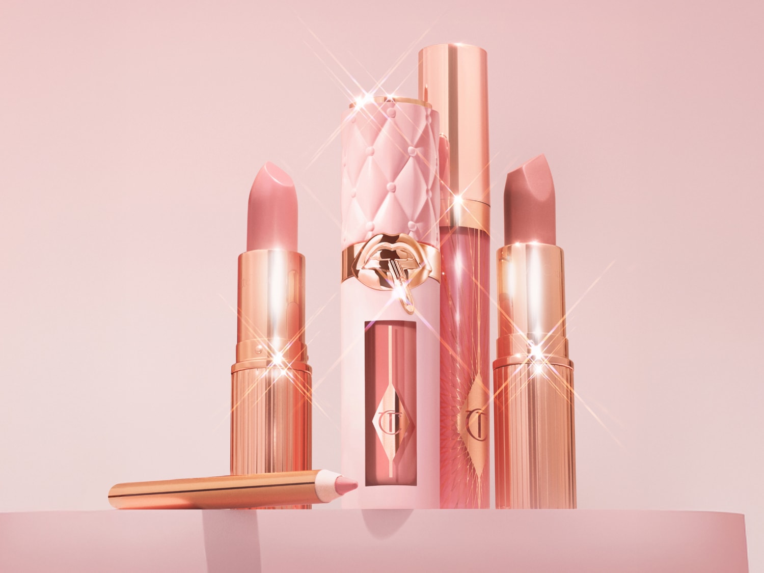 Eine Kollektion von Charlotte Tilbury Lippenprodukten in verschiedenen Rosatönen, darunter Lippenstifte, Lipgloss und Lipliner, die auf einem rosa Hintergrund präsentiert werden.