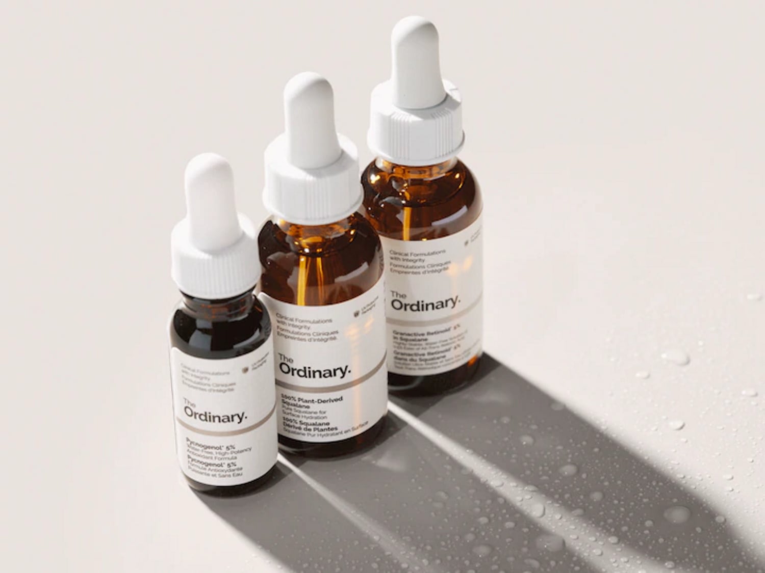 Voici trois flacons de sérum The Ordinary : deux sont de couleur ambrée et un est plus foncé, chacun avec une étiquette blanche et un compte-gouttes blanc.