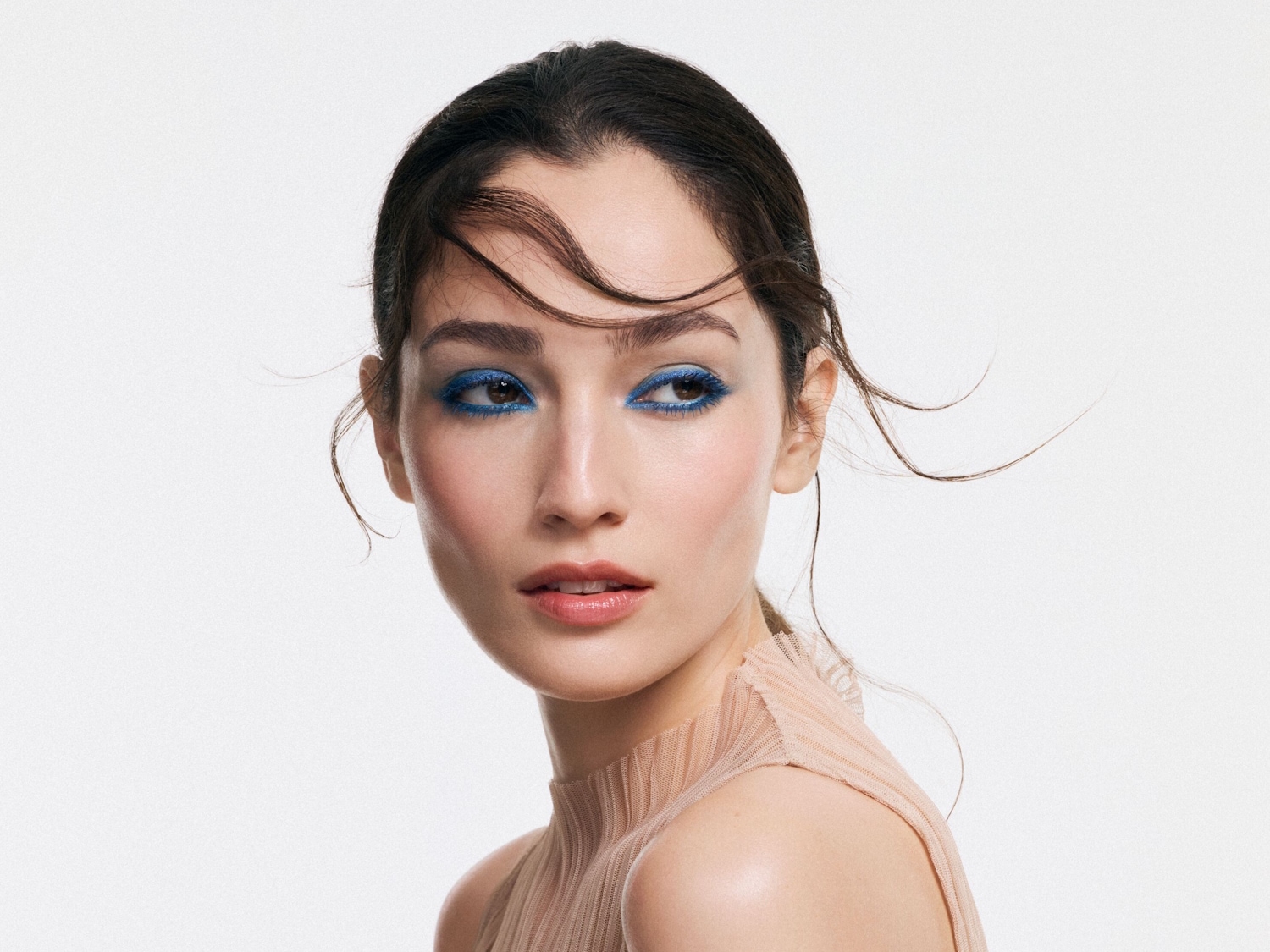 Nahaufnahme einer Frau mit strahlend blauem Lidschatten, der ihre Augen betont, und einem zarten rosa Lippenstift, der ihren natürlichen Teint hervorhebt.