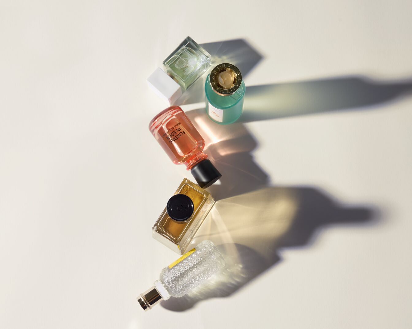 Verschiedene Parfümflaschen in verschiedenen Formen und Farben liegen auf einem hellen Hintergrund und werfen Schatten.