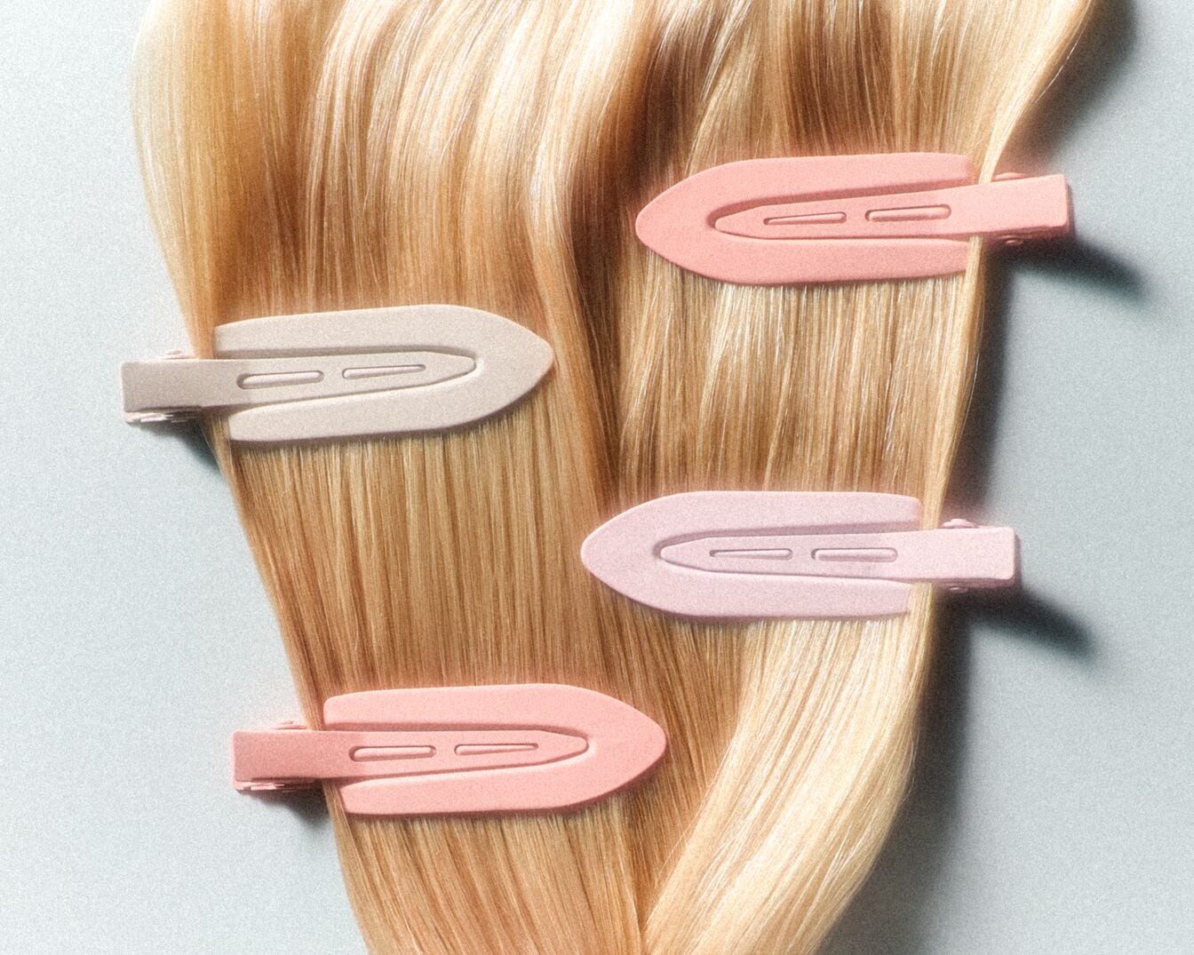 Nahaufnahme von blonden Haaren, die mit vier pastellfarbenen Haarspangen in Rosa- und Beigetönen befestigt sind.