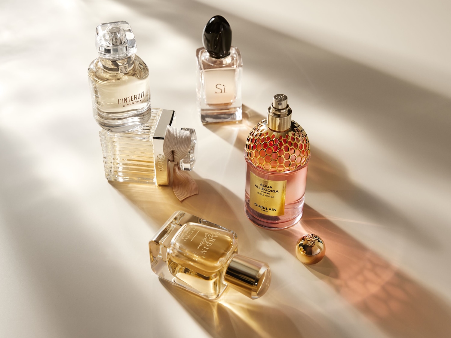 Eine Sammlung von Parfümflakons verschiedener Marken wie Givenchy, Chloé und Guerlain, die auf einer hellen Oberfläche angeordnet sind und deren elegante Designs und subtile Farbnuancen zur Geltung bringen.