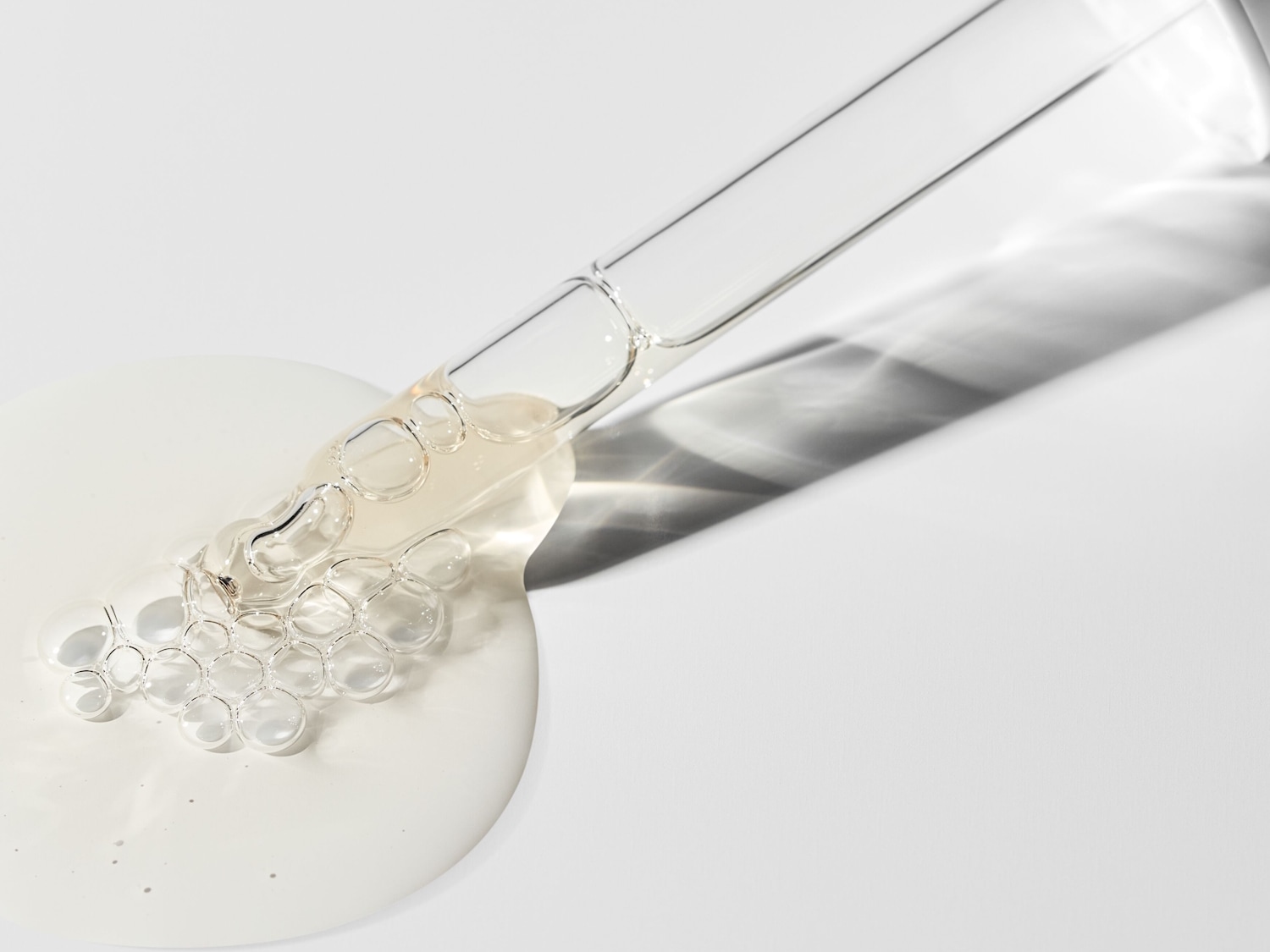 Nahaufnahme einer Pipette mit Serum, das auf einer weißen Oberfläche liegt und eine klare, leicht gelbliche Flüssigkeit mit Luftblasen zeigt.