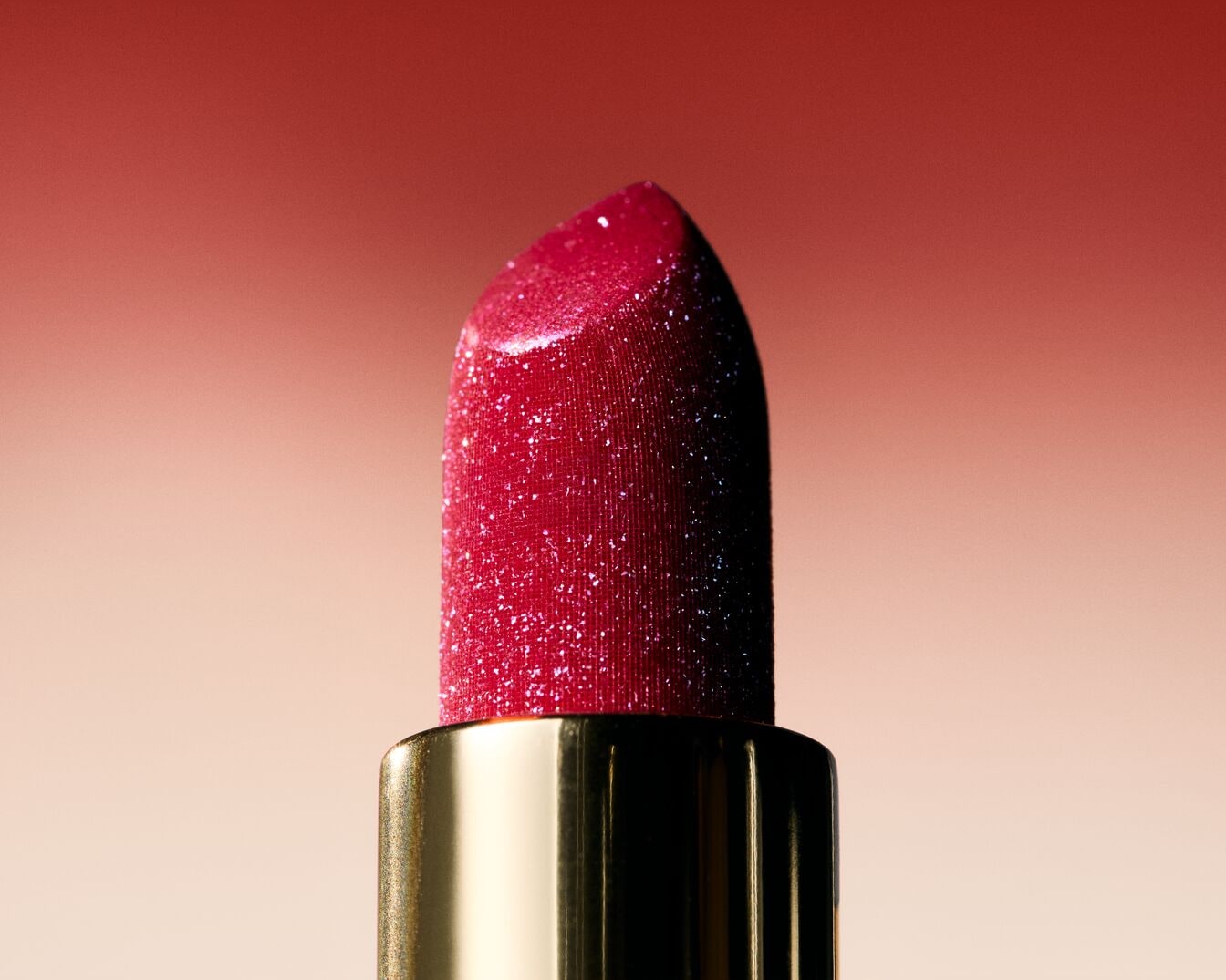 Ryškiai raudonas lūpų dažas auksinėje tūbelėje su blizgučiais suteikia putlumo ir spindesio.