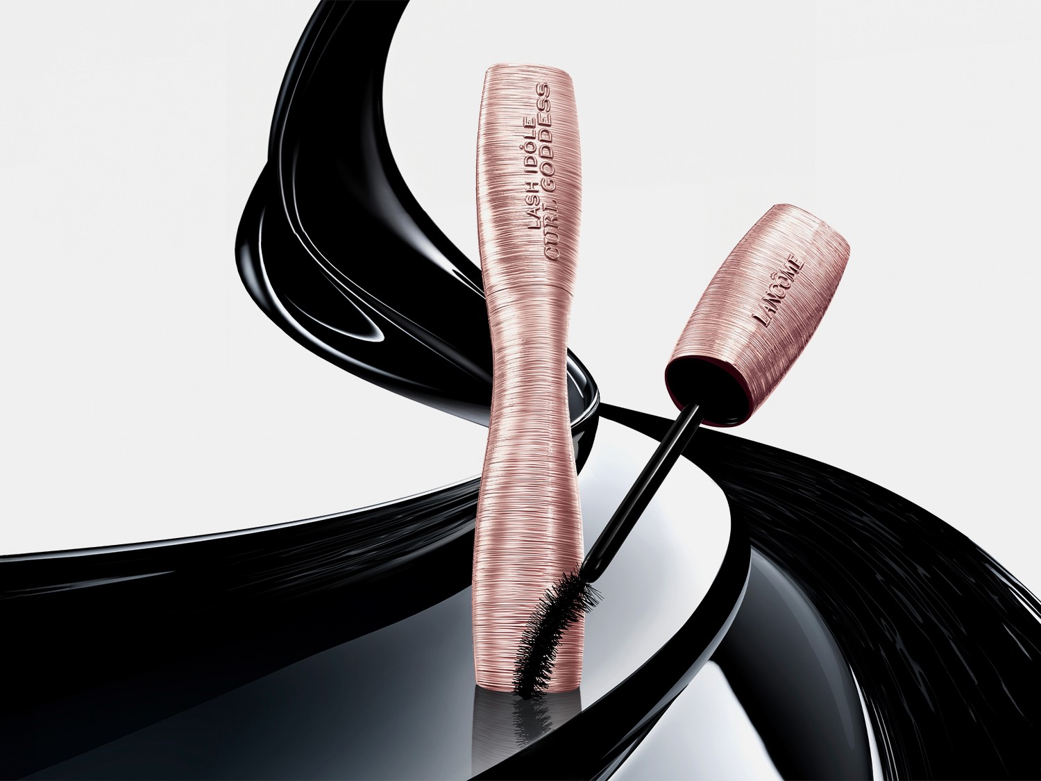 Die Lancôme Lash Idôle Curl Goddess Mascara in einer eleganten, gerippten Roségold-Verpackung mit einer geschwungenen schwarzen Textur im Hintergrund.