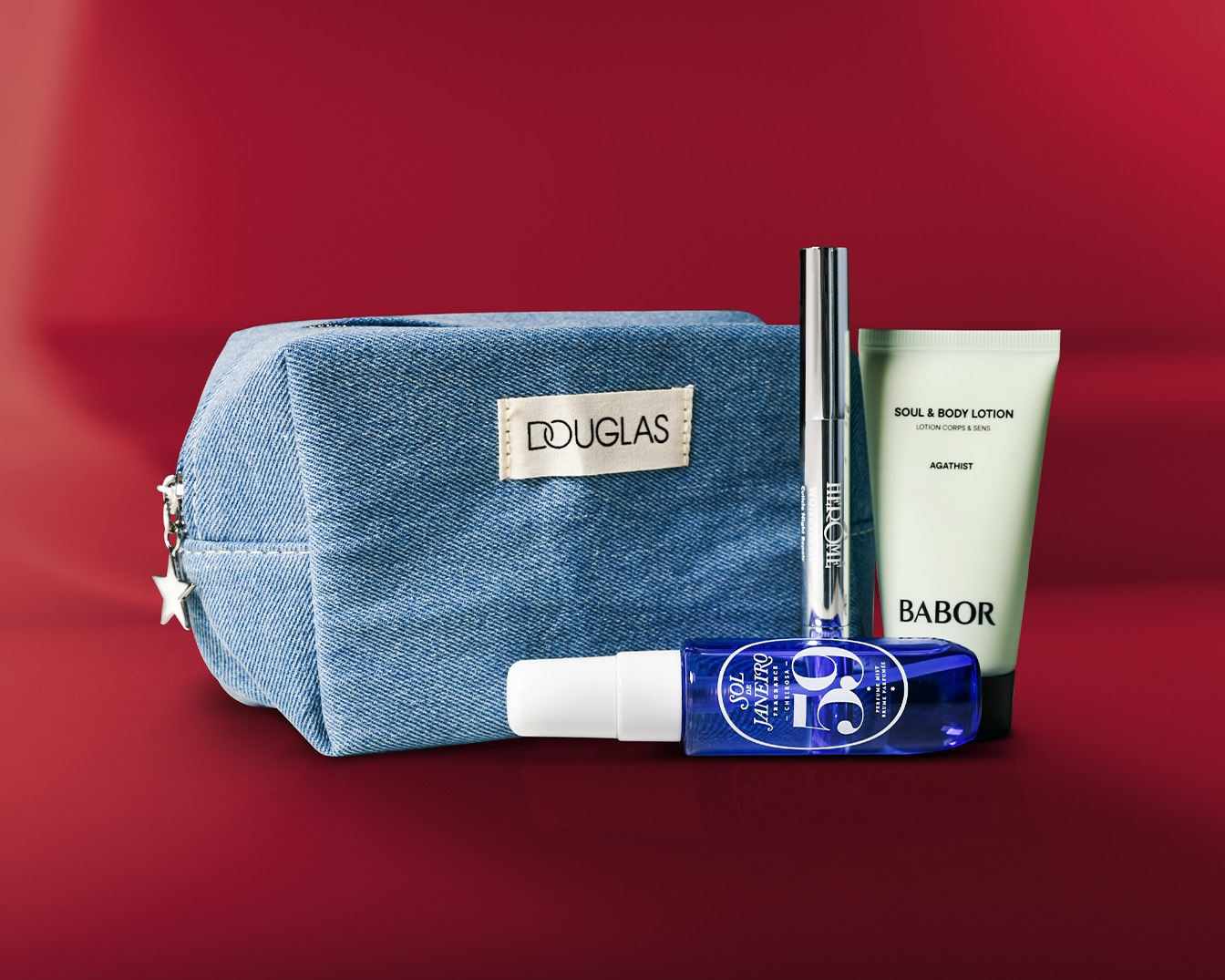 Een blauwe Douglas toilettas van denimstof met een zilveren sterbedel, samen met een zilveren Herome nagelverharder, een blauwe Sol de Janeiro parfumnevel en een witte Babor bodylotion.