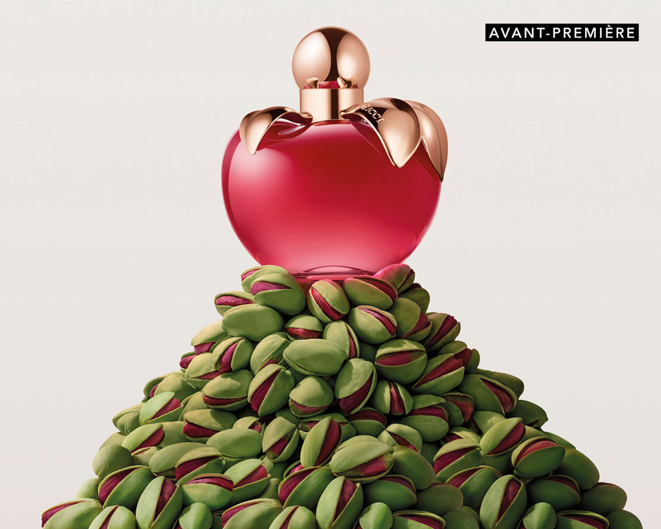 Découvrez Avant-Première : Un parfum Nina Ricci dans un flacon rouge en forme de pomme, perché sur une montagne de pistaches.