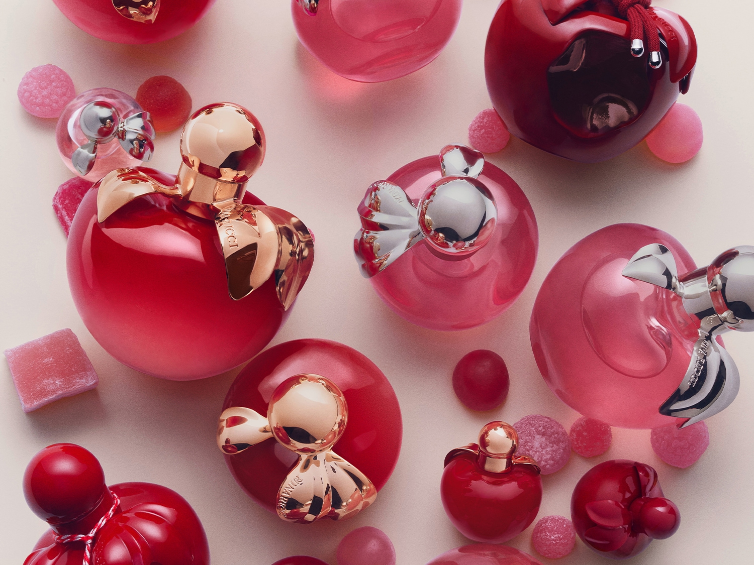 Découvrez les parfums Nina Ricci dans leurs flacons en forme de pomme rouge et rose, parsemés de bonbons colorés.