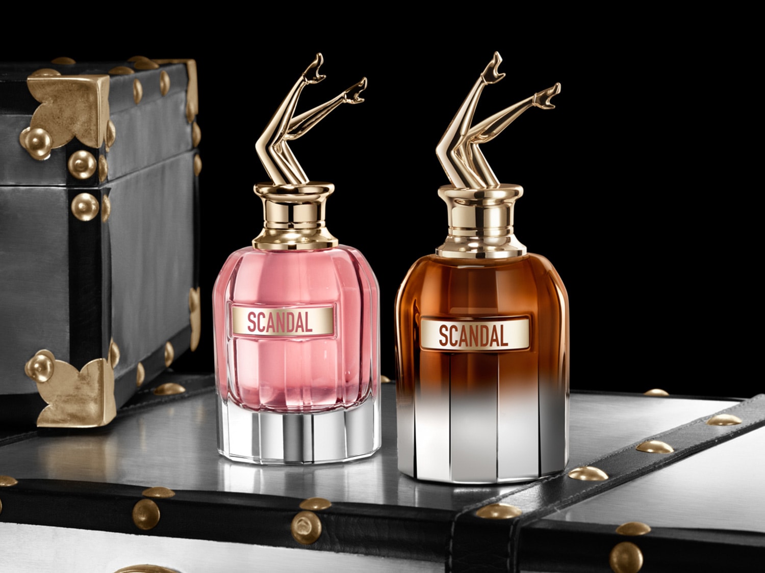 Découvrez Scandal, un parfum captivant présenté dans un flacon rose et ambré orné de jambes dorées, évoquant luxe et audace.