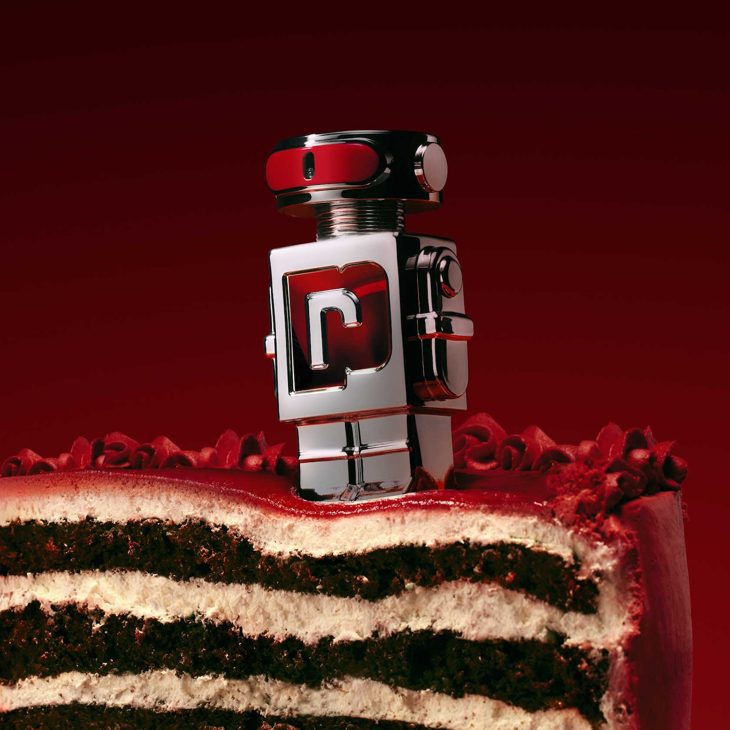 Un parfum robotique argenté et rouge trône sur une part de gâteau au chocolat à plusieurs étages, le tout sur un fond rouge foncé.