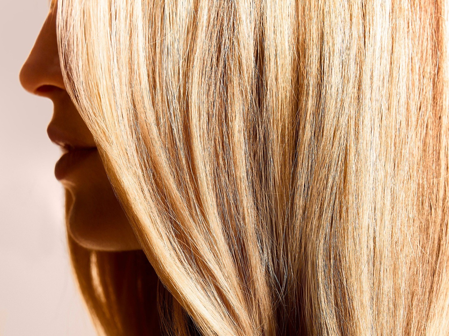 Nahaufnahme von glattem, blondem Haar, das teilweise das Gesicht einer Person bedeckt und einen Blick auf Nase und Lippen freigibt.