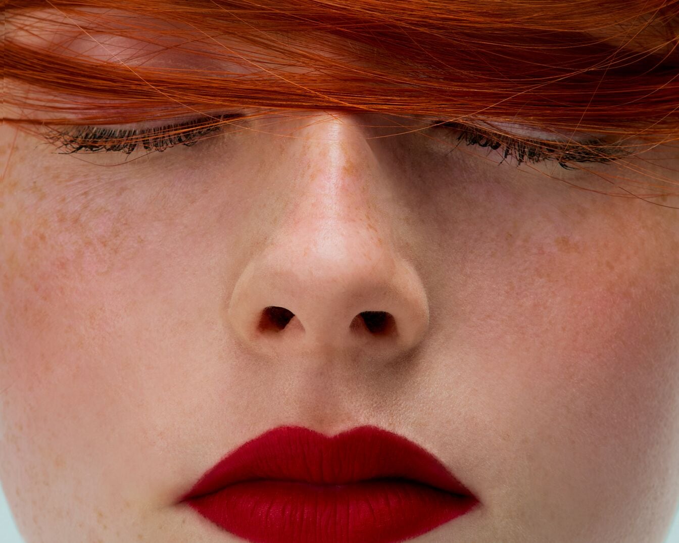 Nahaufnahme eines Frauengesichts mit roten Lippen und roten Haaren, die über die Augen fallen, wodurch ein auffälliger und moderner Look entsteht.