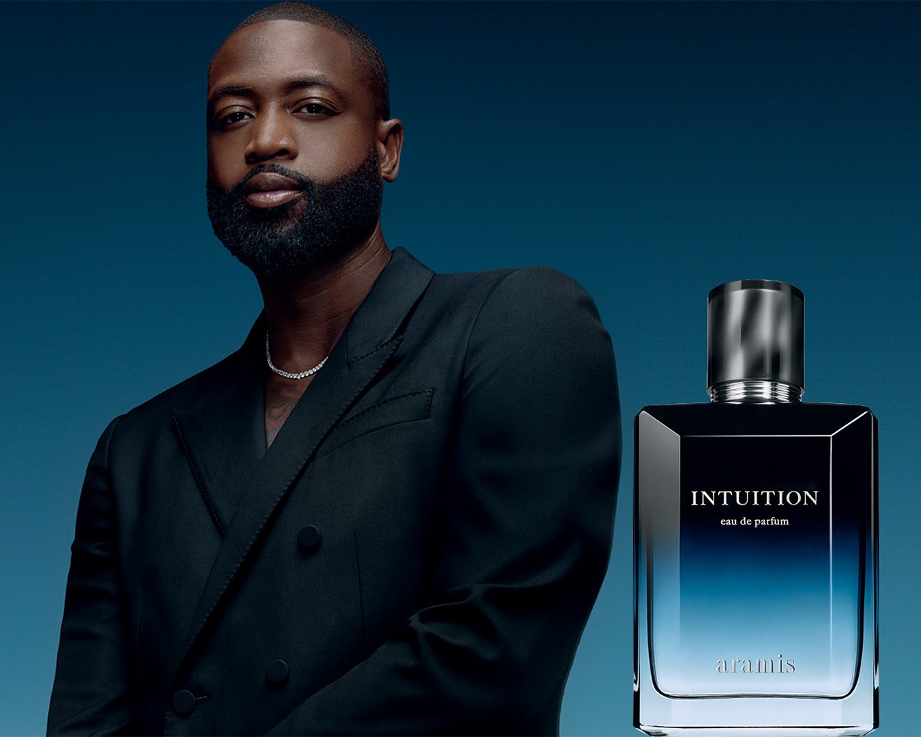 Een foto van een man met een zwarte blazer en een zilveren ketting, naast een fles Aramis Intuition eau de parfum met een zwart-blauwe kleurverloop.