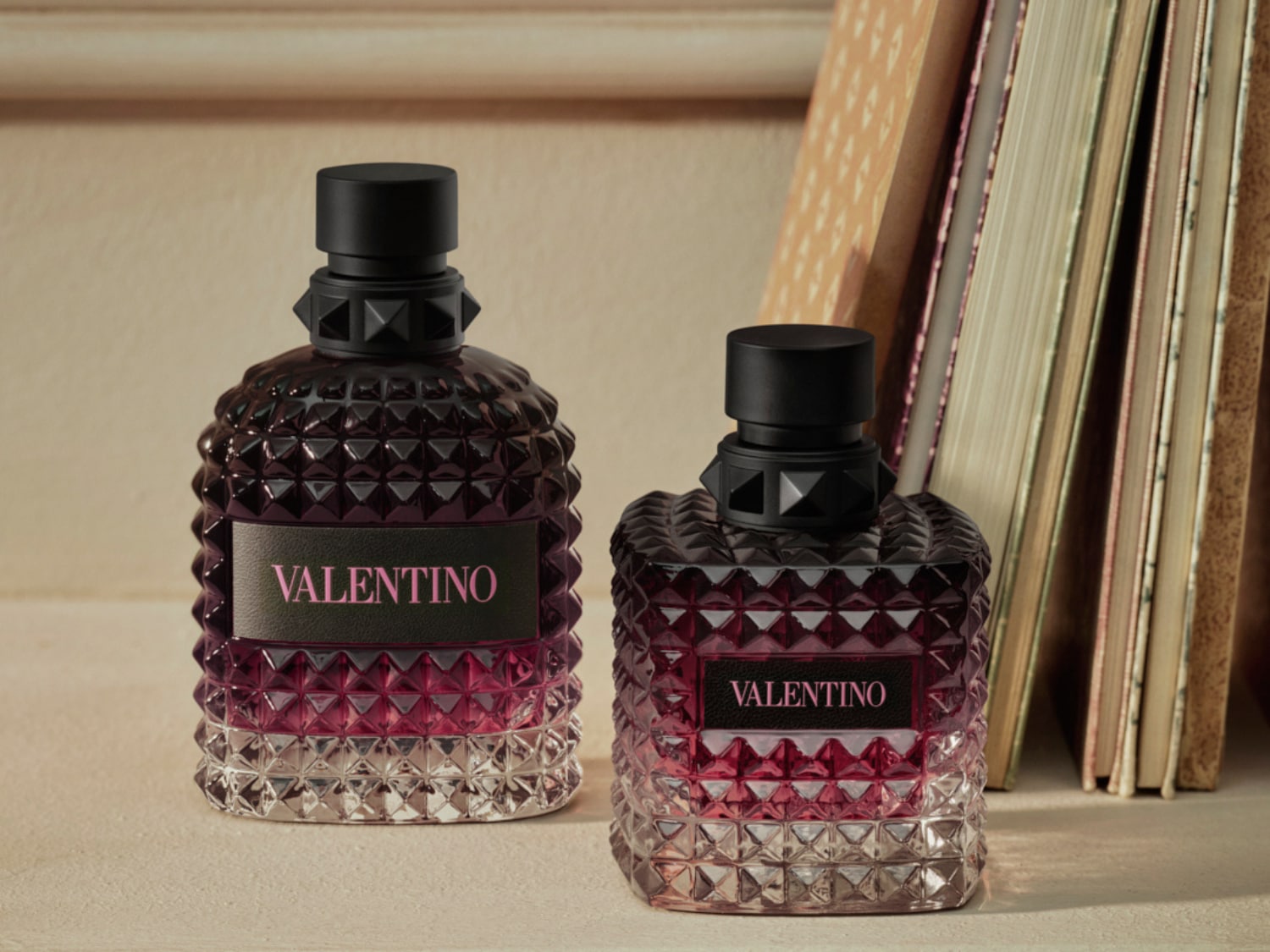 Két Valentino parfümös üveg látható, egy nagyobb és egy kisebb, mindkettő sötét rózsaszín árnyalatú, fekete kupakkal és rózsaszín VALENTINO felirattal.