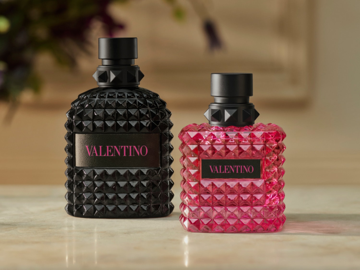 Két Valentino parfümös üveg látható: egy fekete és egy rózsaszín, mindkettőn a „Valentino” felirat olvasható rózsaszín betűkkel.