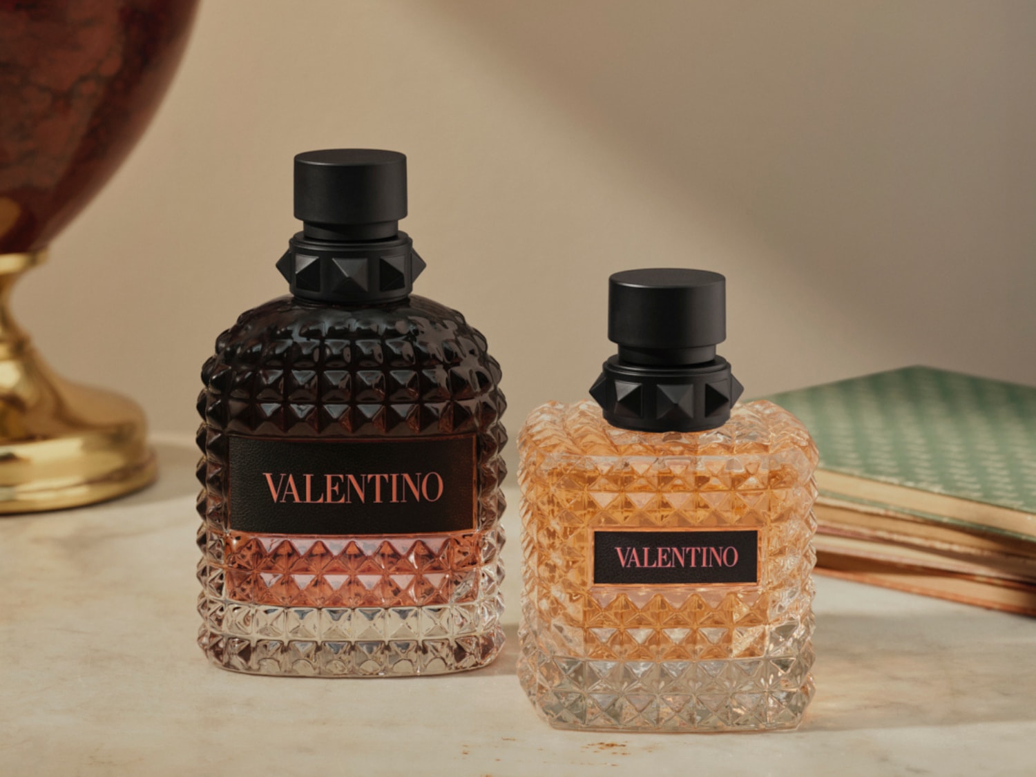 Két Valentino parfümös üveg látható, az egyik sötét, a másik világosabb borostyánszínű folyadékkal, mindkettő fekete kupakkal és a Valentino felirattal.