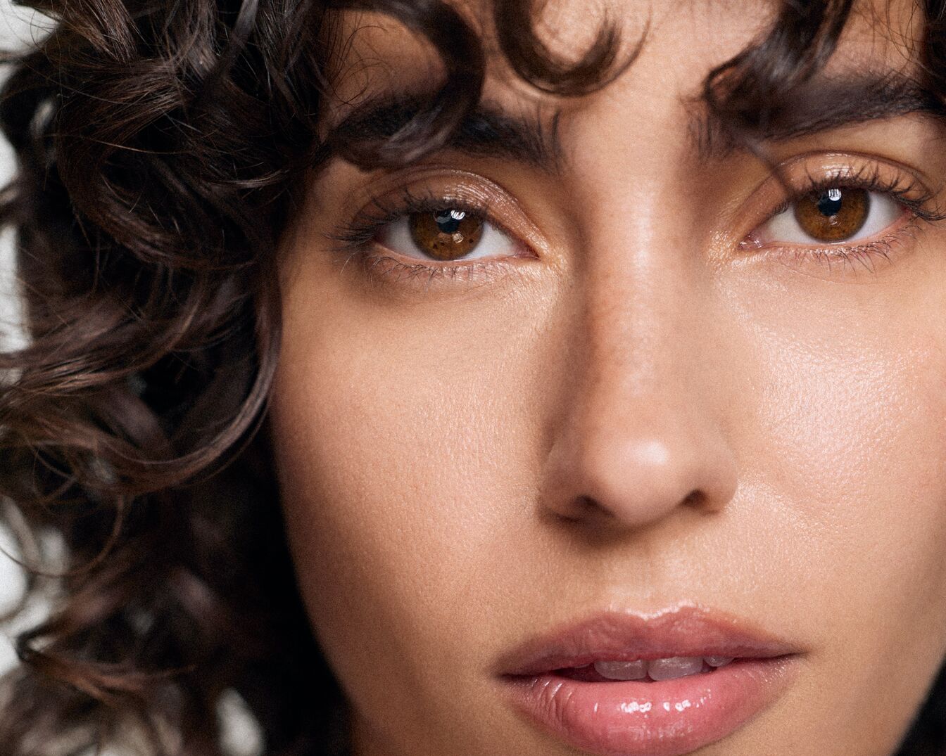 Nahaufnahme eines Frauengesichts mit braunen Augen, lockigem, dunklem Haar und glänzenden Lippen.