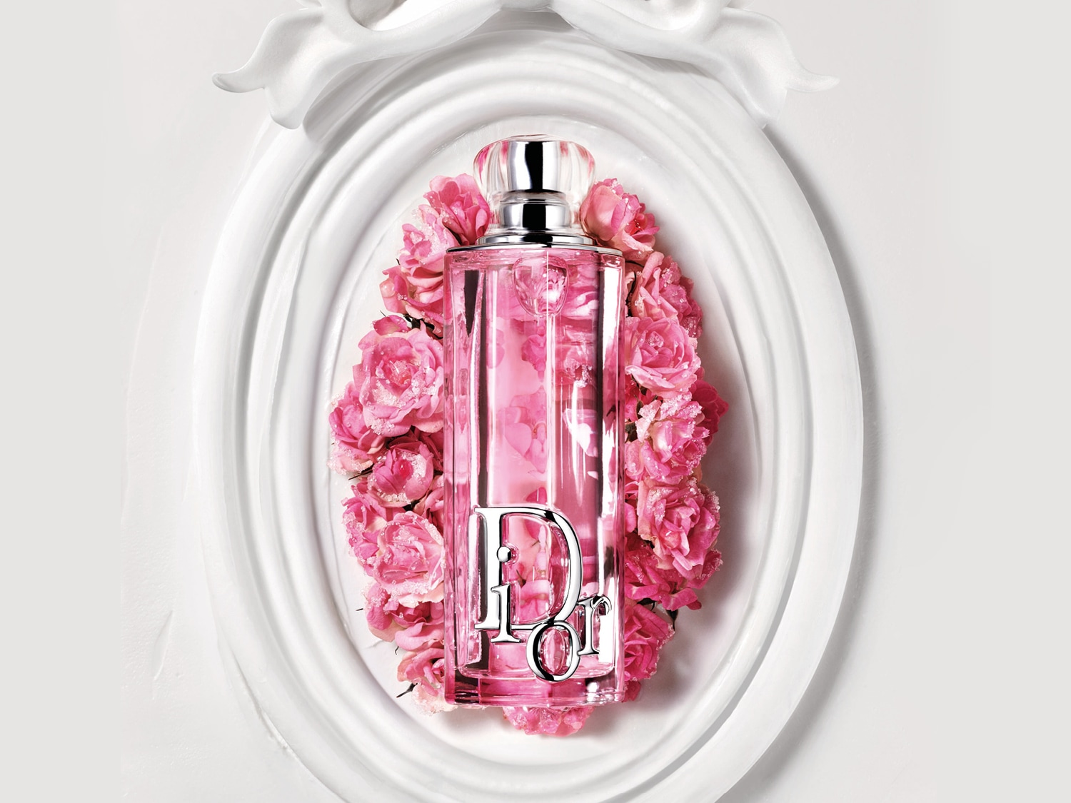 Un flacone di profumo Dior rosa chiaro è circondato da rose rosa, il tutto incorniciato in una cornice bianca decorativa.