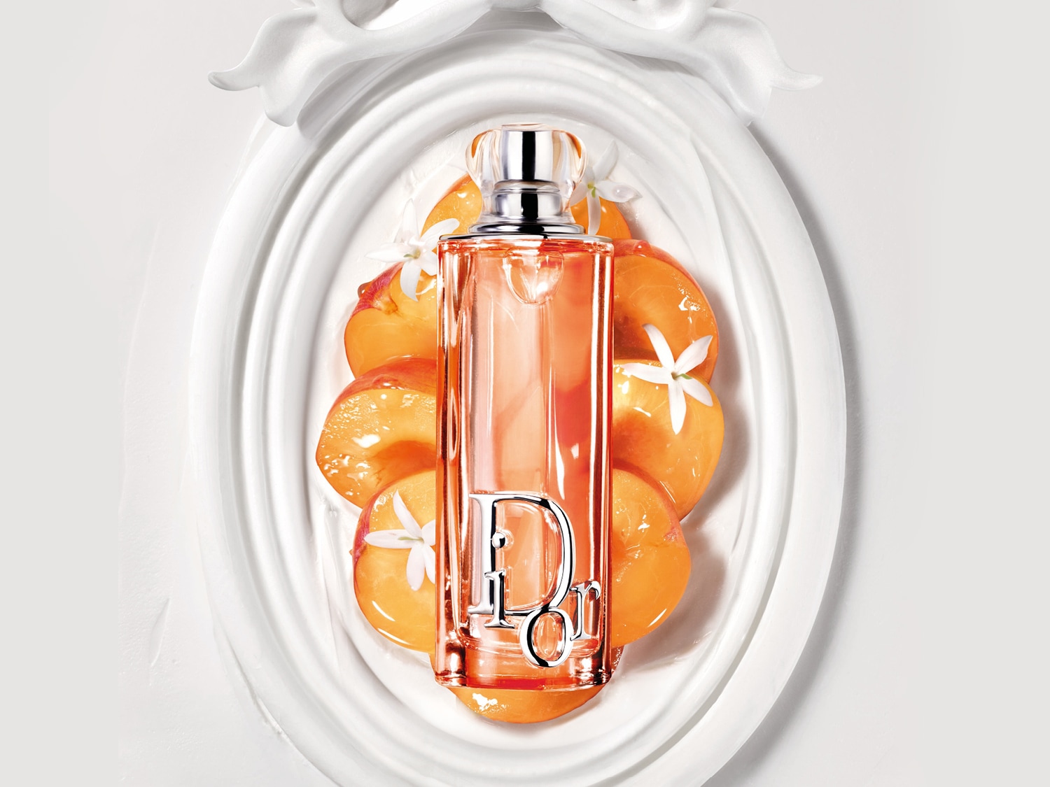 Il profumo Dior color pesca è adagiato su fette di pesca e decorato con fiori bianchi, il tutto su un elegante vassoio bianco.