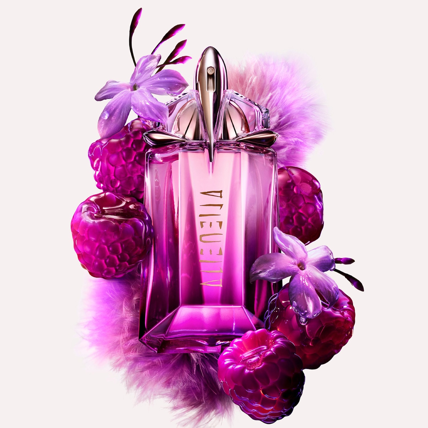 Butelka różowych perfum Alien otoczona malinami, kwiatami i piórami tworzy luksusową kompozycję.