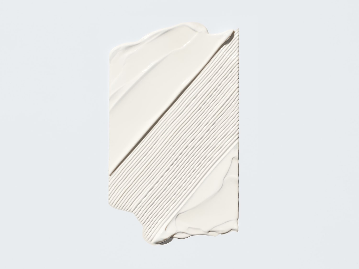 Šviesiai kreminės spalvos kosmetikos priemonės tepinėlis su lygiomis linijomis ant balto paviršiaus.