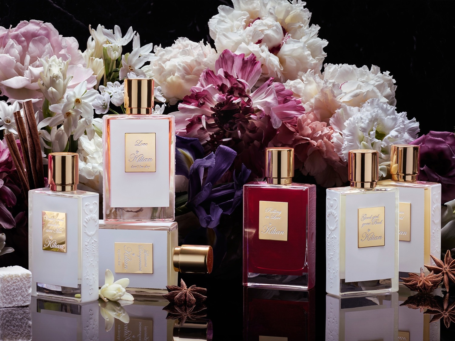 Ontdek de Kilian parfumcollectie, met flessen variërend van helder tot dieprood, elk met gouden accenten en omringd door een weelderige bloemenzee.