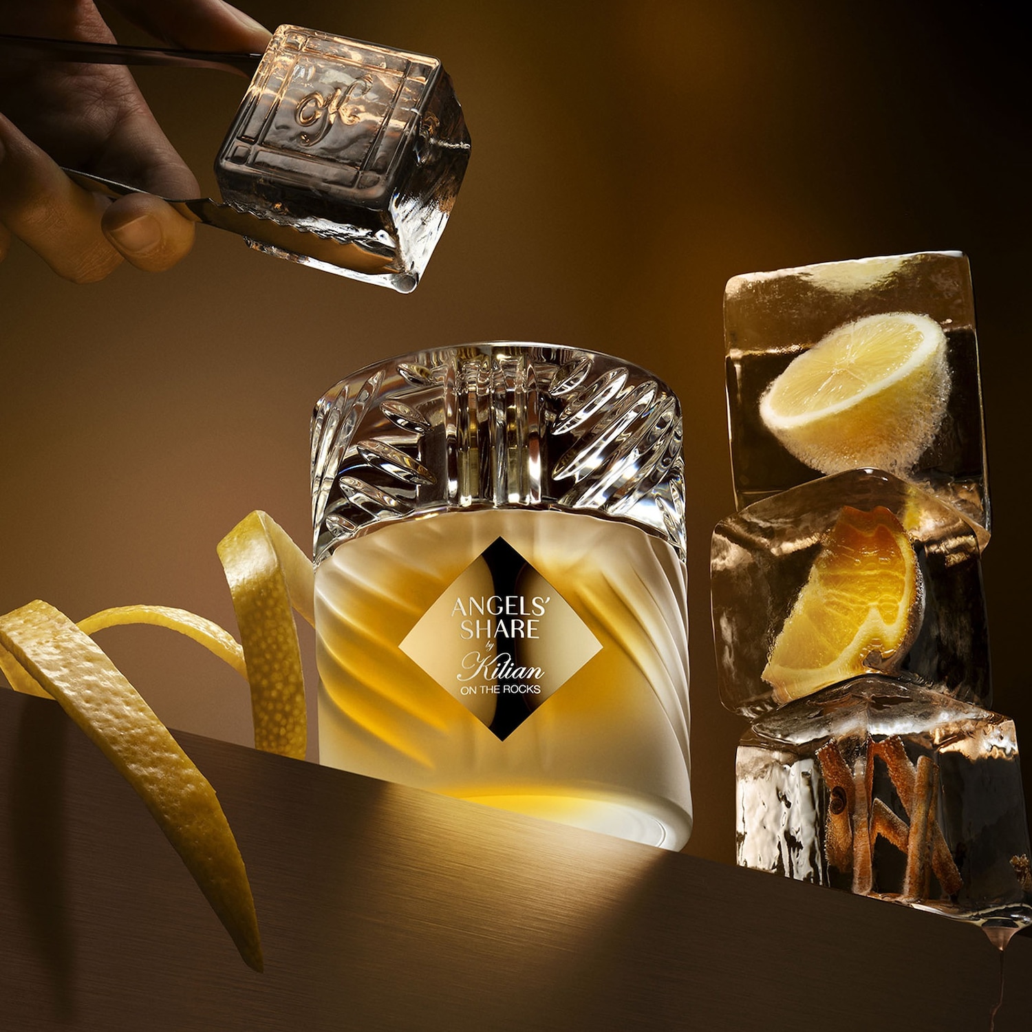 De Kilian Angel's Share on the Rocks parfumfles staat centraal, omringd door ijsblokjes met citroen en sinaasappel, en een hand die een ijsblokje vasthoudt, wat een verfrissende en luxueuze sfeer creëert.