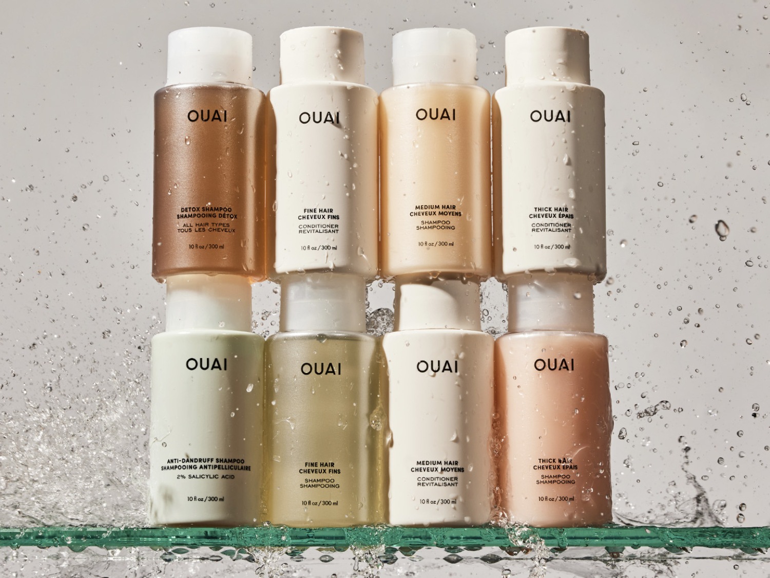 Gestapelde OUAI haarverzorgingsproducten, waaronder detoxshampoo, conditioner voor fijn en dik haar, en antiroosshampoo, allemaal in witte flessen met zwarte tekst.