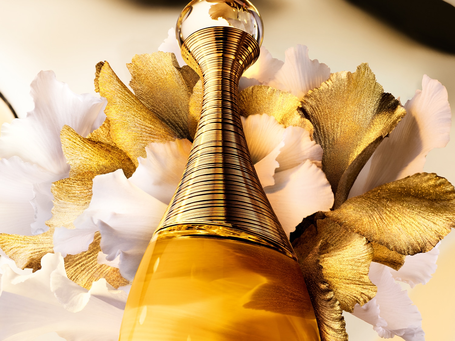 Gouden parfumfles van Dior J'adore, omringd door witte en gouden bloemblaadjes, straalt luxe en elegantie uit.