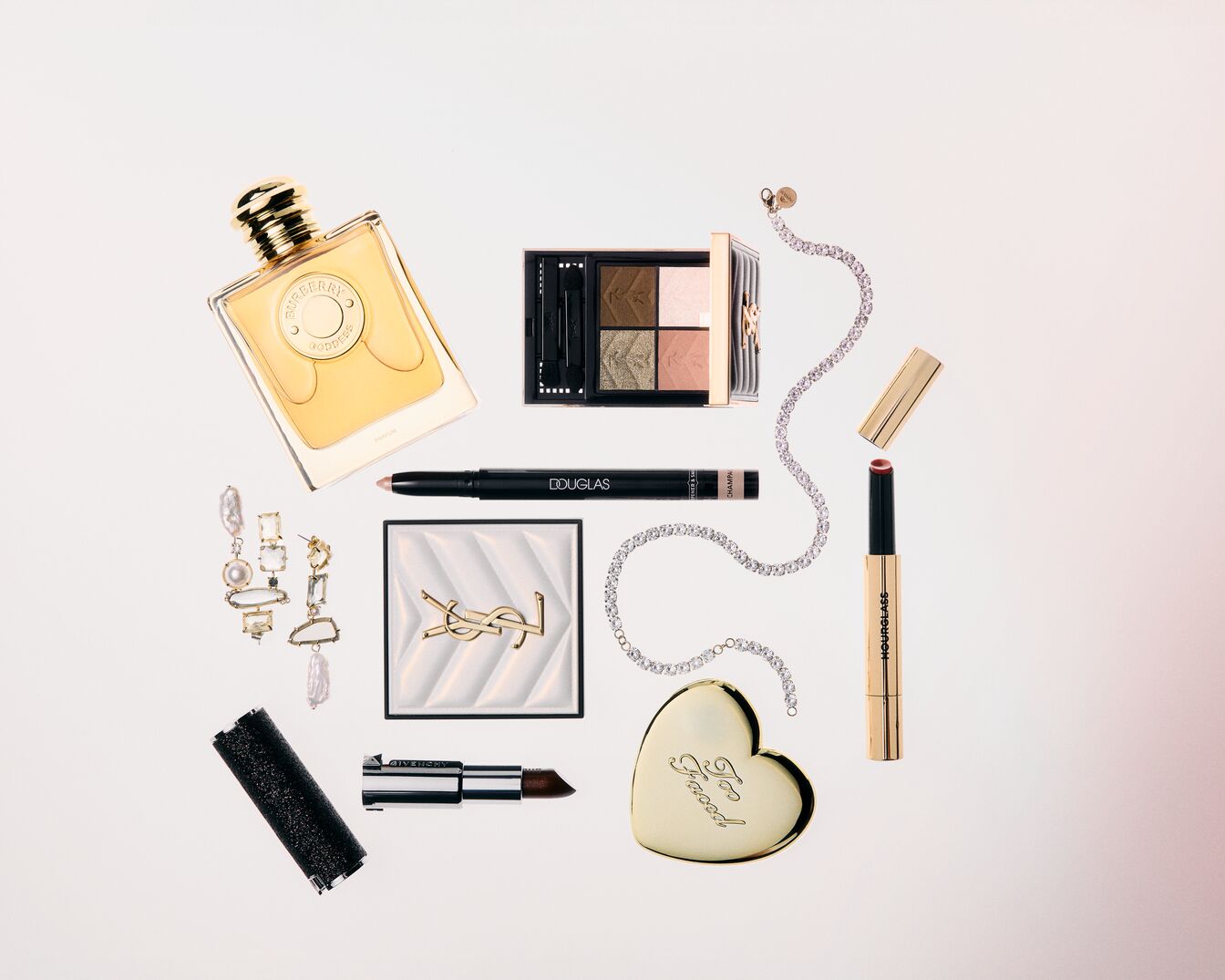 Elegancki zestaw kosmetyków i biżuterii, w tym perfumy Burberry Goddess w bursztynowym flakonie, paleta cieni do powiek, szminka i błyszczący naszyjnik.