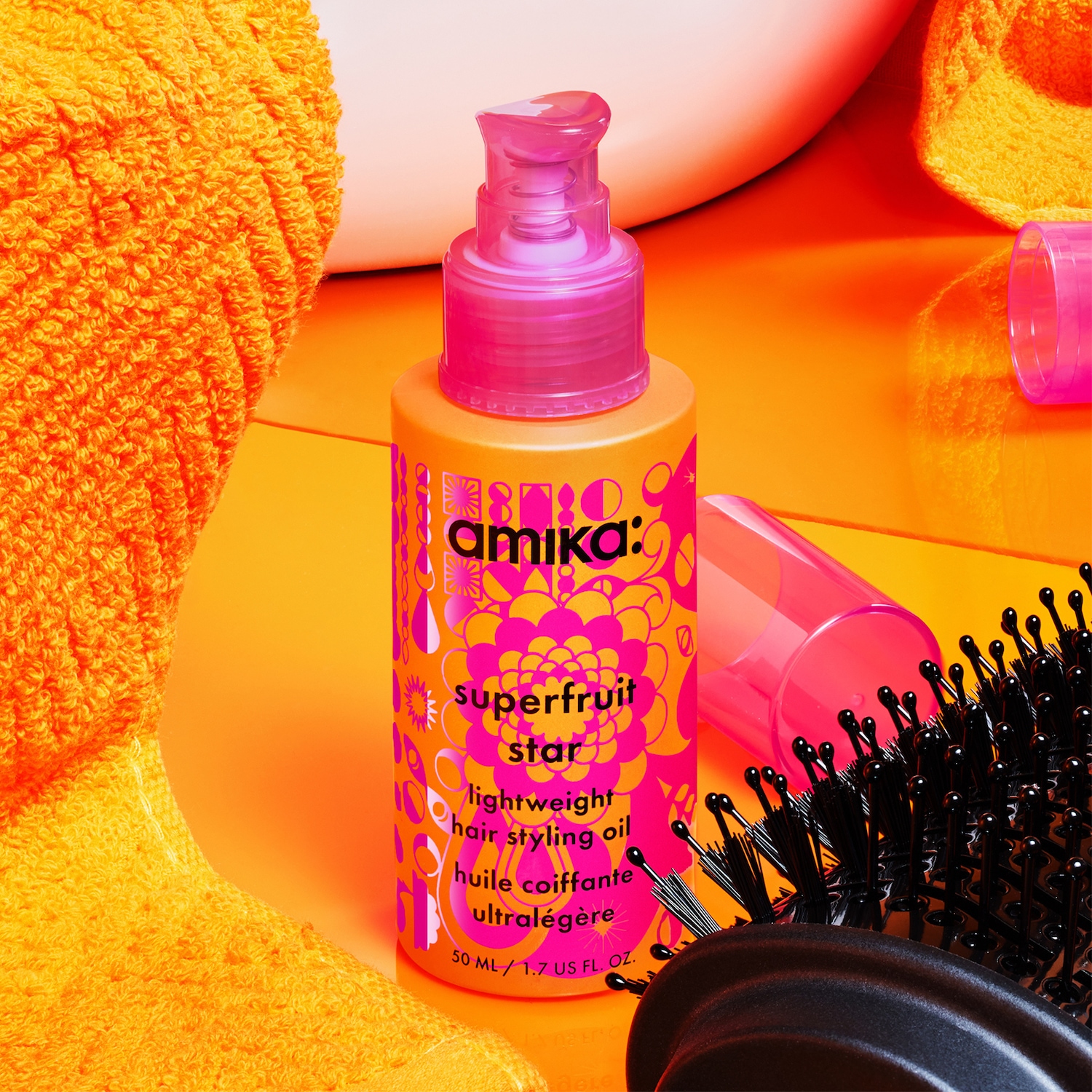 Voici l'huile coiffante légère Superfruit Star d'Amika, présentée dans un flacon orange vif avec des accents floraux roses.