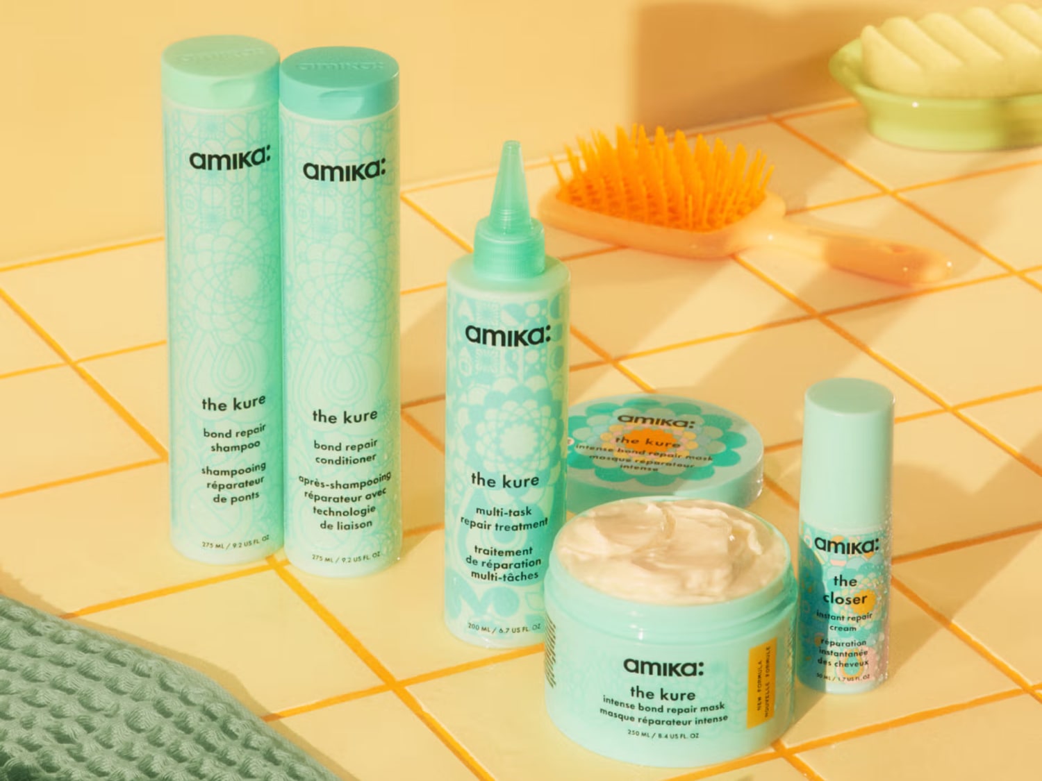 Découvrez la gamme Amika The Kure dans des emballages turquoise : shampooing, revitalisant, traitement, masque et crème réparatrice pour des cheveux revitalisés.