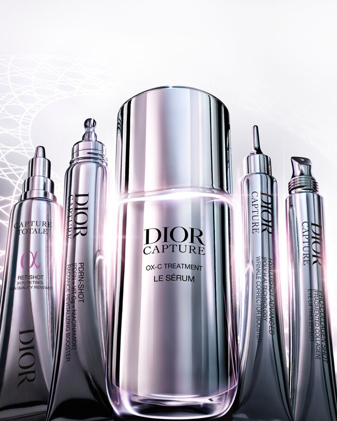 Cinco productos Dior Capture, incluyendo suero, potenciadores y tratamientos, se presentan en envases plateados y brillantes, destacando el suero OX-C Treatment Le Sérum en el centro.