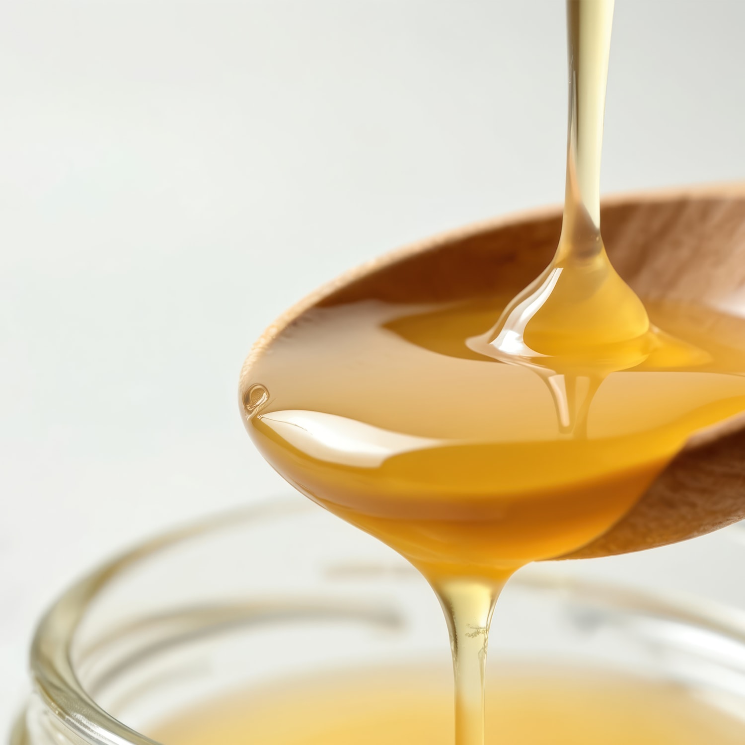 Nahaufnahme von goldenem Honig, der von einem Holzlöffel in ein Glas tropft und die fließende Textur und Süße betont.