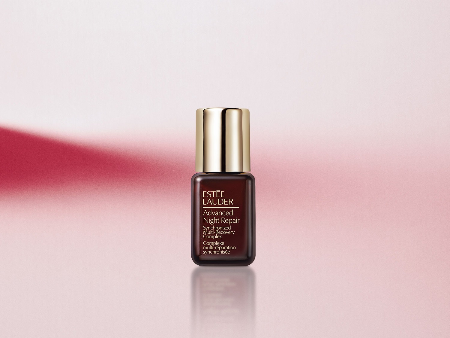 Nahaufnahme einer kleinen, dunkelbraunen Flasche Estée Lauder Advanced Night Repair mit goldenem Verschluss vor einem sanften rosa Hintergrund.