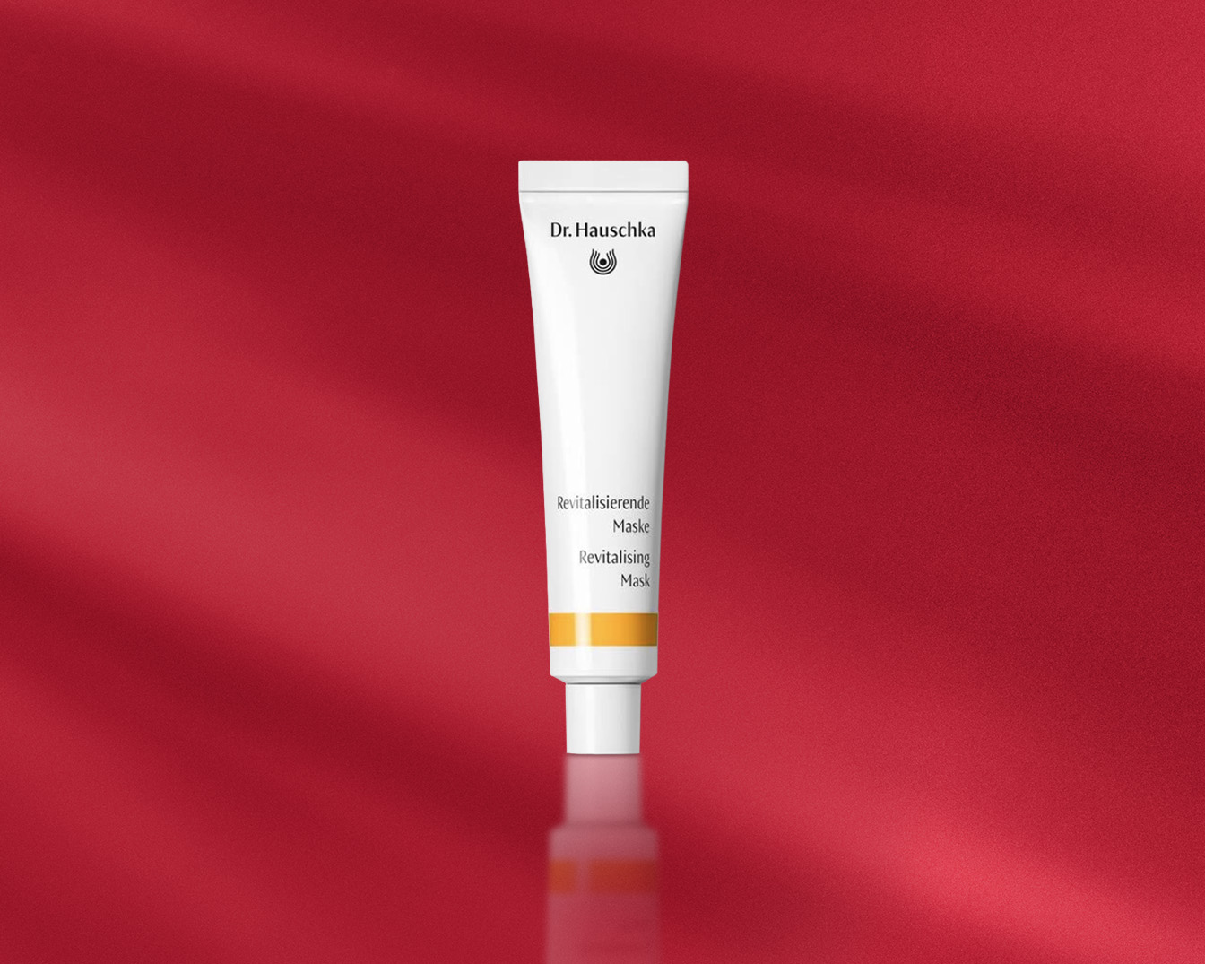 Dr. Hauschka Revitalisierende Maske in einer weißen Tube mit einem gelben Streifen auf einem roten Hintergrund.
