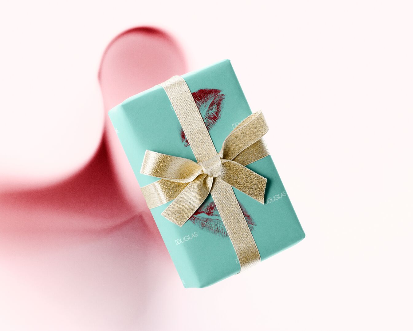 Un cadeau Douglas élégamment emballé dans un papier bleu turquoise, orné d'un ruban doré scintillant et d'un motif de baiser rouge, flottant sur un fond rose doux.