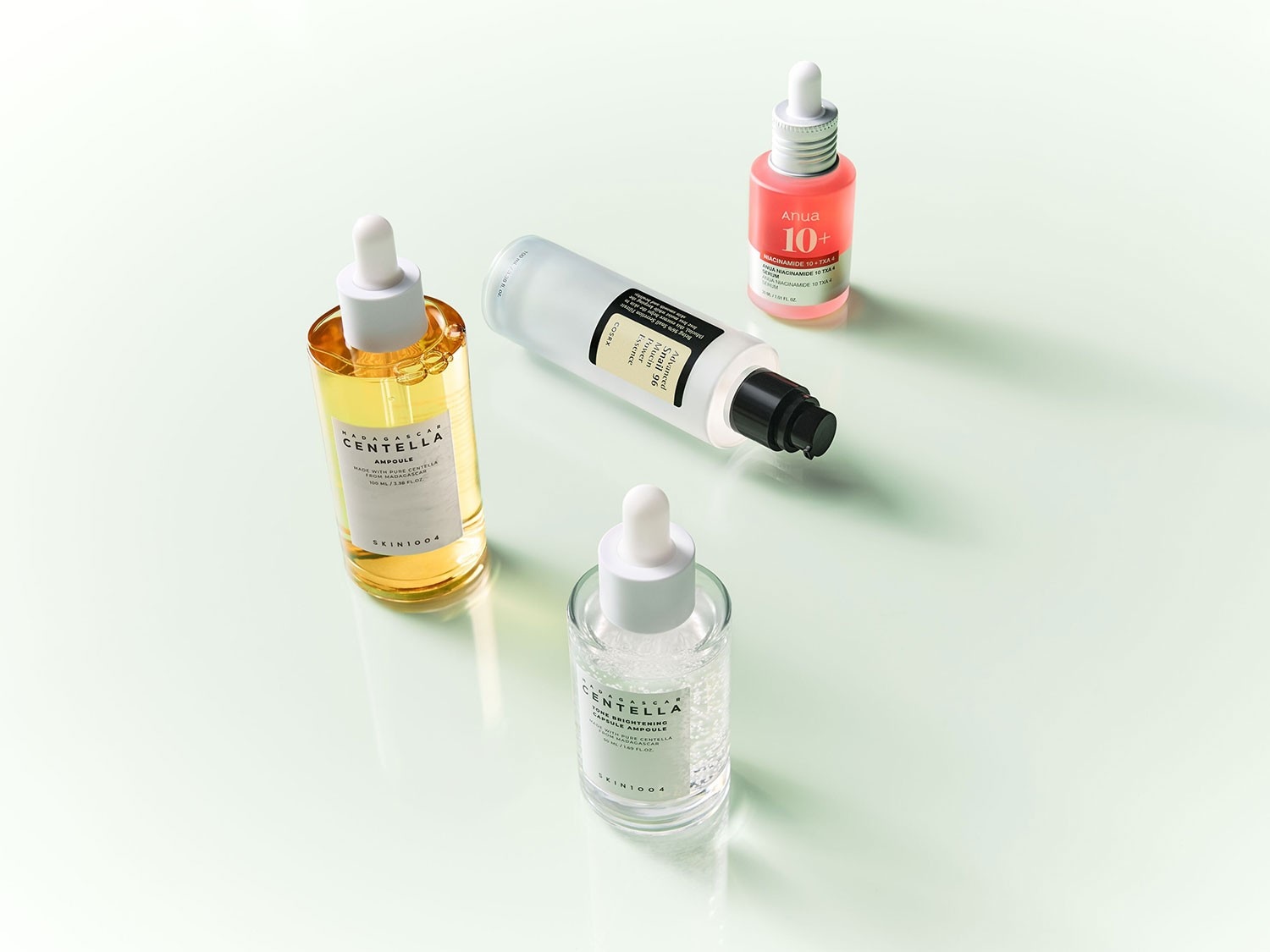 Verschiedene Hautpflegeprodukte, darunter Skin1004 Centella Ampulle mit Gelbton, COSRX Advanced Snail 96 Mucin Power Essence in Weiß und Anua 10+ Niacinamid 10 TXA Serum in Rosa.