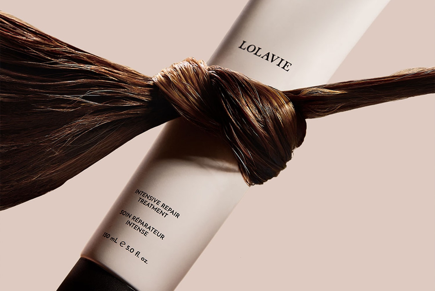 Le traitement réparateur intensif LOLAVIE, présenté dans un tube blanc épuré, est mis en valeur par une mèche de cheveux bruns nouée autour, promettant une réparation intense pour vos cheveux.