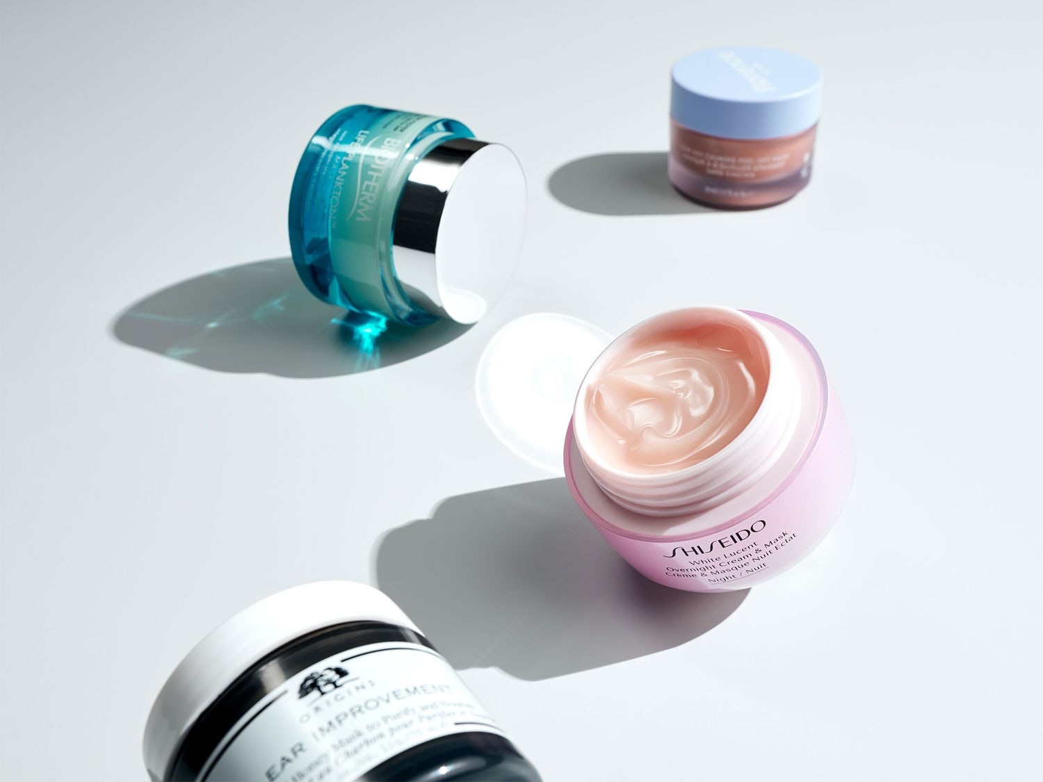 Eine Nahaufnahme von verschiedenen Hautpflegeprodukten, darunter Biotherm Life Plankton, Origins Clear Improvement Maske und Shiseido White Lucent Nachtcreme, die auf einer hellen Oberfläche angeordnet sind.